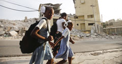 School children walk through streets of rubble