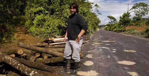 man standing alongside logs felled from the Ecuadorian jungle 