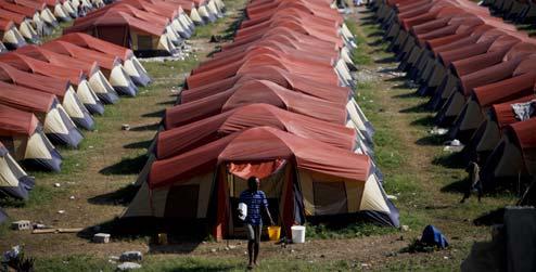 A man carrying a bucket in front of rows of tents in Haiti