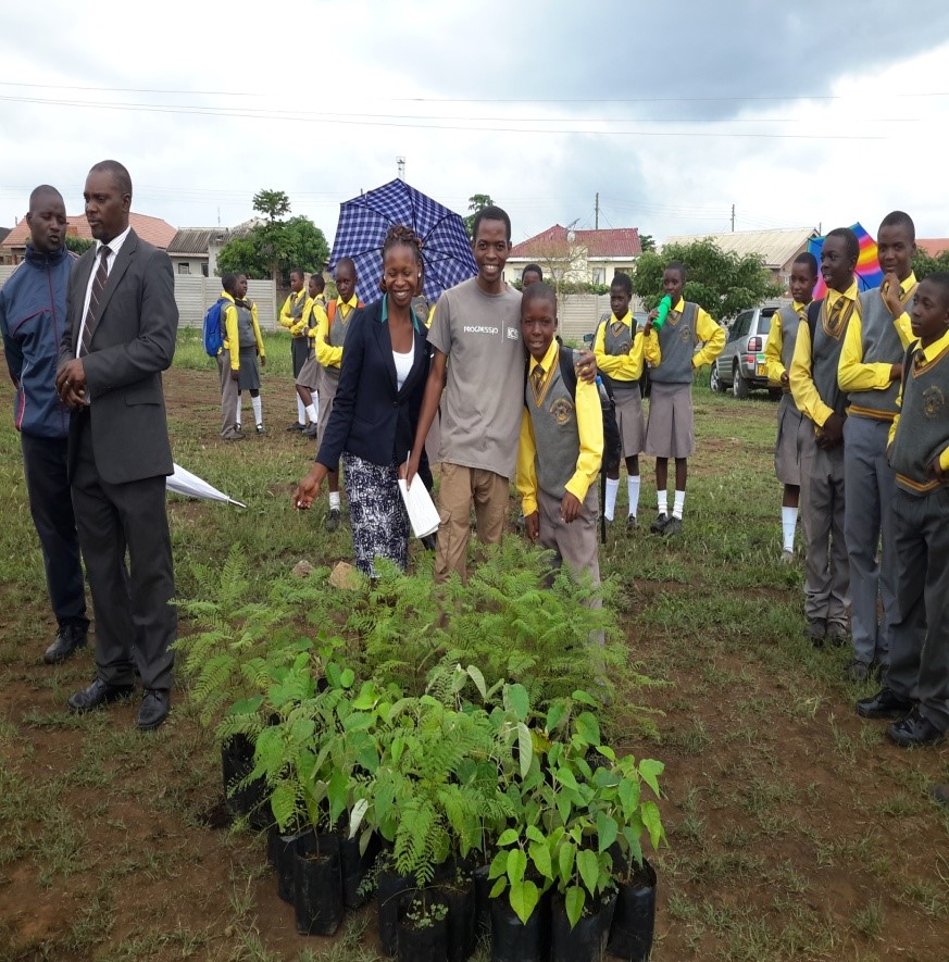 A female teacher and male volunteer stand in front of the donated trees