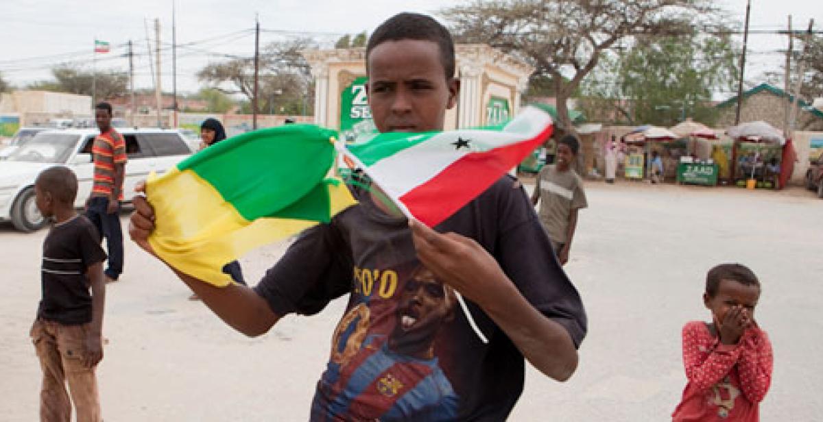 A young man holds flags on a Hargeisa street