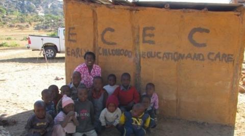 A Zimbabwean teacher sits in front of her school with he4r pupils