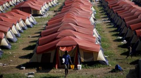 A man carrying a bucket in front of rows of tents in Haiti