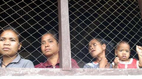 Women look through a wire screen at a window in Timor-Leste